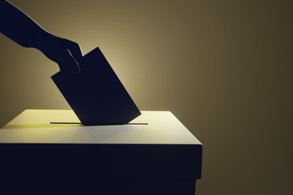 Silhouette of a hand putting a vote into the voting box on pale yellow background