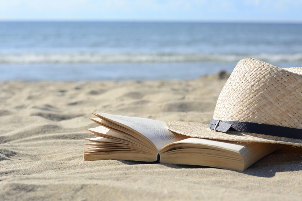 A book on the beach with a hat beside it