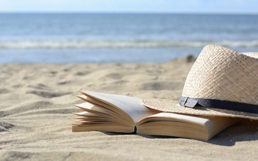 A book on the beach with a hat beside it