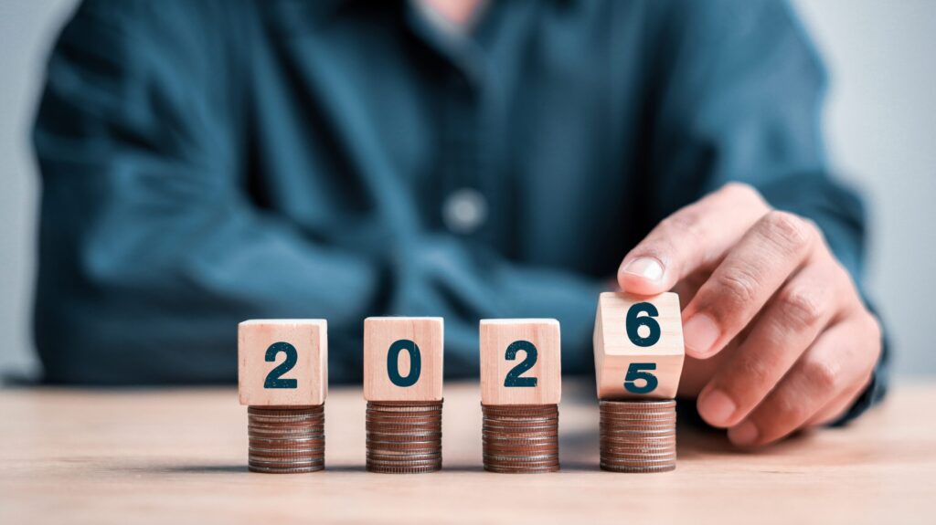 A man in a dark blue shirt has a 2025 in front of him made from playing blocks. He is rolling the 5 to become a 6.
