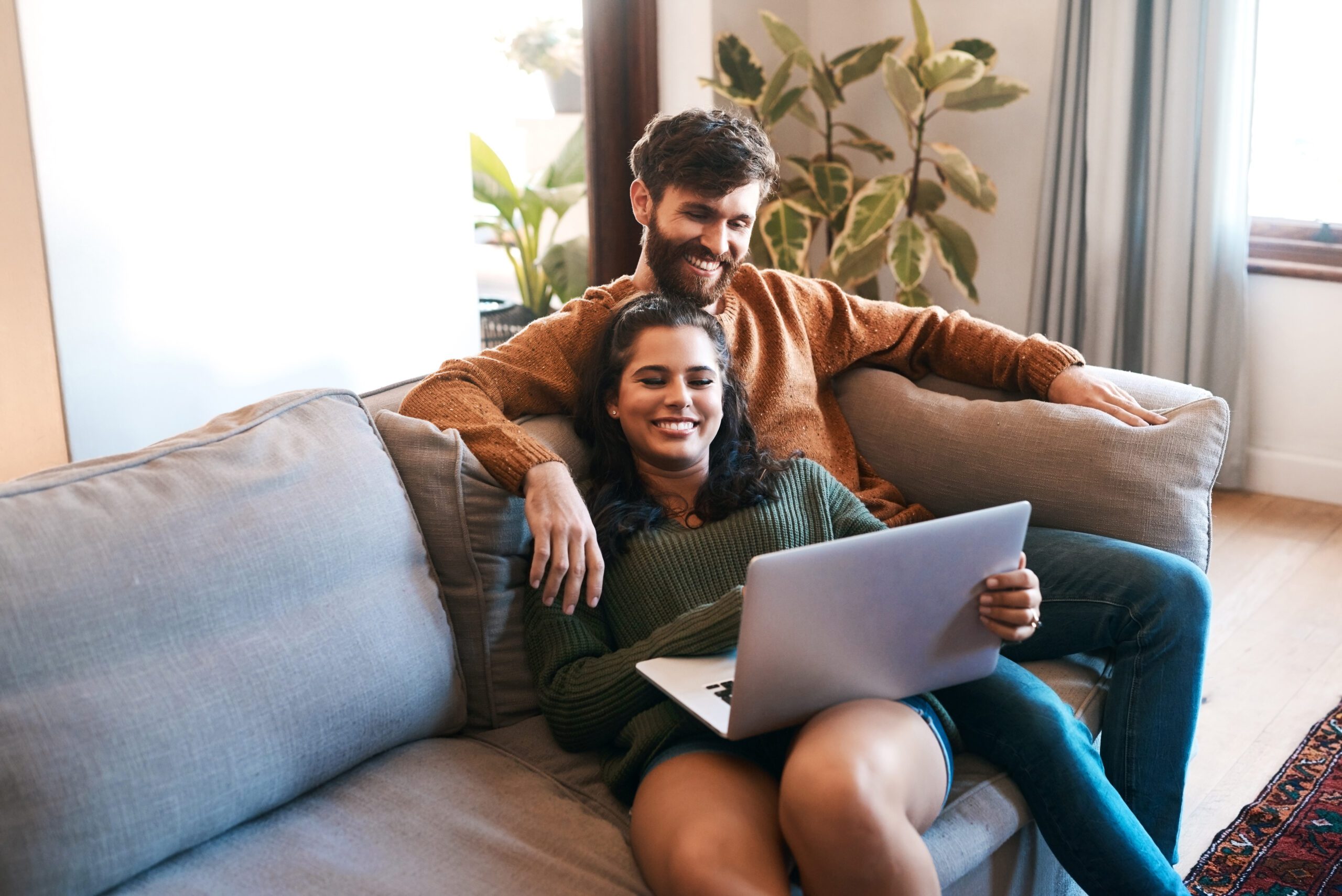 Smiling couple at home on a couch, reading an ebook on a laptop